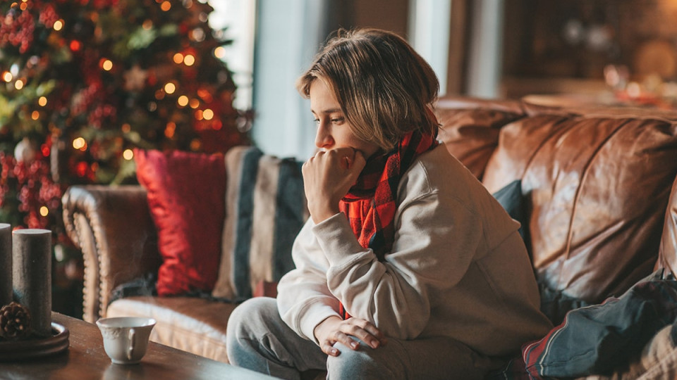 somber woman sitting on the couch in front of a christmas tree
